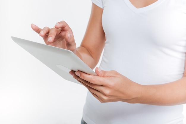 Bijgesneden foto van jonge vrouw met digitale tablet geïsoleerd op een witte muur