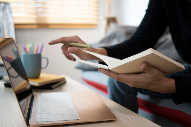 Bijgesneden geschoten man die notitie maakt op notebook en informatie zoekt op laptop.