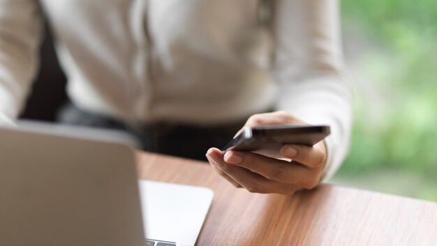 Bijgesneden geschoten zakenman die aan laptop werkt en mobiele telefoon op het bureau houdt