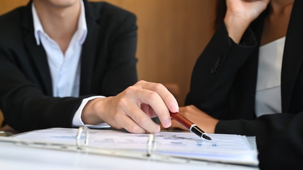 Bijgesneden geschoten zakenman die pen vasthoudt en financiële informatie aan zijn collega uitlegt.