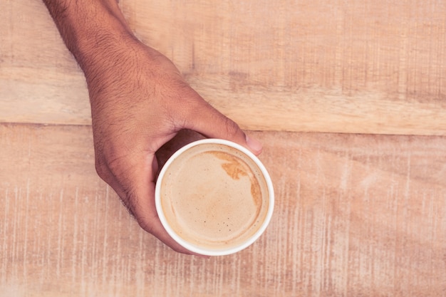 Bijgesneden hand met koffiekopje op houten tafel