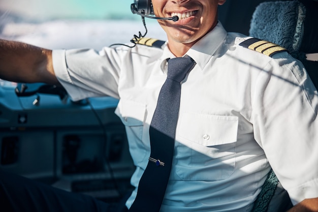 Foto bijgesneden hoofdportret van glimlachende knappe man die in de cockpit zit in professionele oortelefoons klaar om op te stijgen