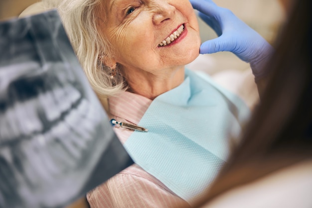 Foto bijgesneden hoofdportret van oudere vrouw die haar tanden laat zien aan de vrouwelijke tandarts terwijl ze overleg heeft met professionele specialist