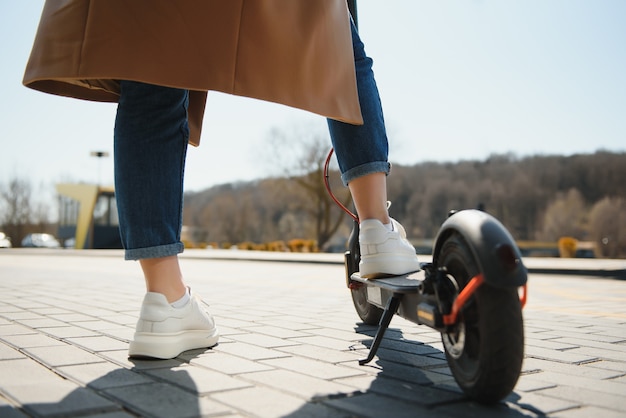 Foto bijgesneden op vrouw benen voeten rijden op elektrische kick scooter in de stad