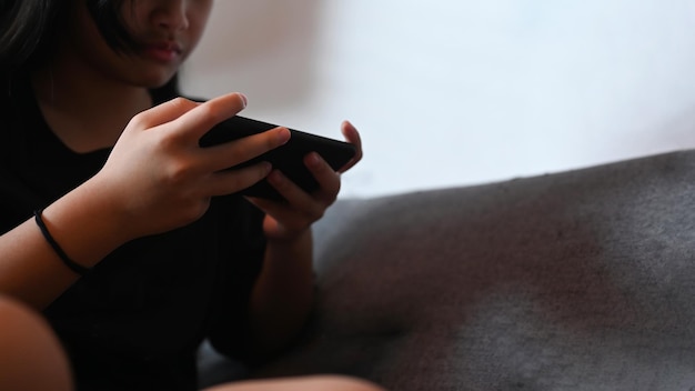 Bijgesneden opname Aziatisch meisje dat online games speelt met mobiele telefoon terwijl ze op de bank zit