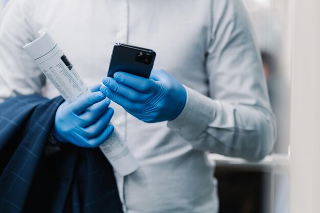 Bijgesneden opname van anonieme man gekleed in wit overhemd medische rubberen handschoenen om coronavirus te voorkomen gebruikt mobiele telefoon downloads nieuwe app houdt krant altijd in contact Griepvirus