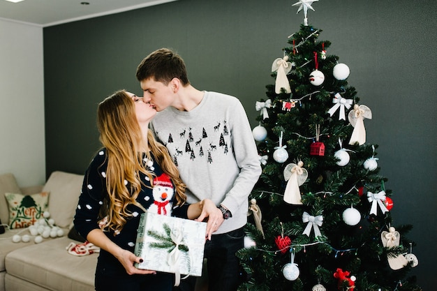 Bijgesneden opname van een man die zijn vriendin verrast met een kerstcadeau in de buurt van een boom. familie geeft huidige doos, night xmas. prettige kerstdagen en fijne feestdagen! familie die geschenken uitwisselt.