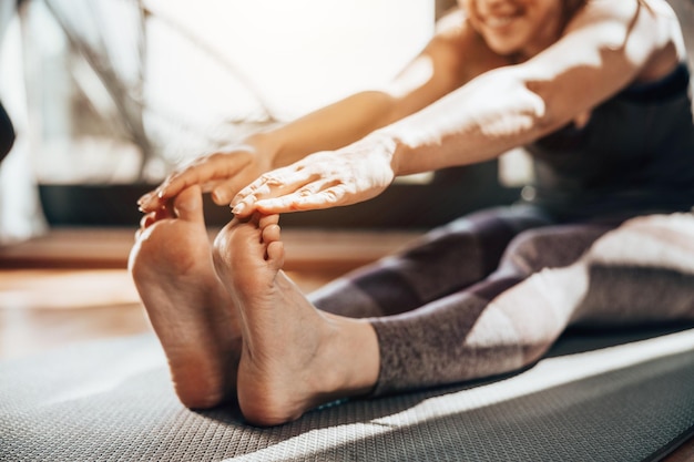 Bijgesneden opname van een ontspannen jonge vrouw die 's ochtends thuis strekkende yoga-oefeningen doet.