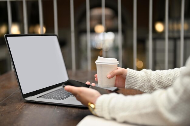 Bijgesneden opname van een vrouw die smartphone gebruikt en een kopje koffie vasthoudt terwijl ze in een café werkt