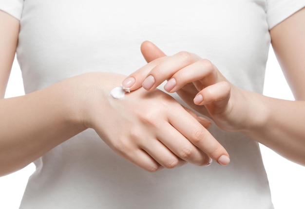 Bijgesneden opname van een vrouw in een wit t-shirt die handcrème aanbrengt op wit wordt geïsoleerd Verzorgde korte natuurlijke nagels