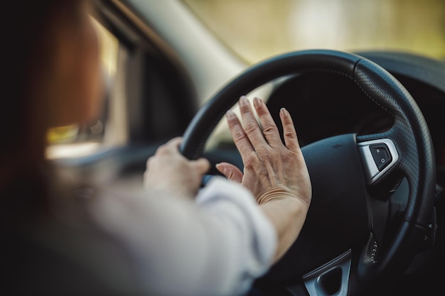 Bijgesneden opname van een zakenvrouw die op de toeter drukt tijdens het autorijden.