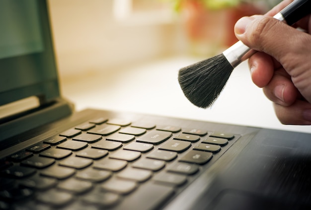 Bijgesneden opname van goede huisvrouw die afstoffen met een kleine bezemlaptop