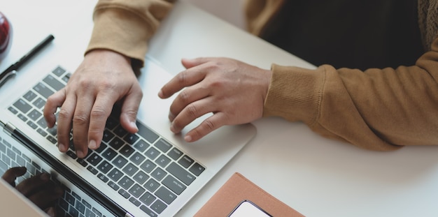 Bijgesneden opname van jonge man te typen op laptopcomputer tijdens het werken aan zijn project