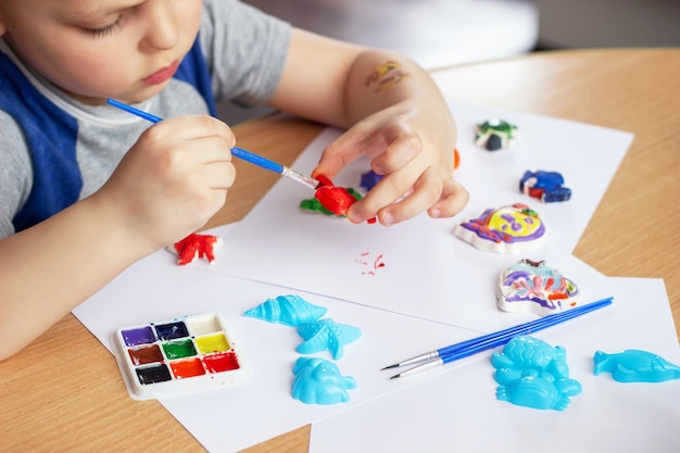 Bijgesneden opname van kind dat gipsfiguren kleurt met gekleurde verf met een penseel Creativiteit voor kinderen