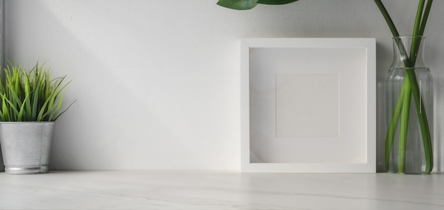 Bijgesneden opname van minimale werkruimte met mock up frame en boom pot op witte houten tafel en witte muur achtergrond