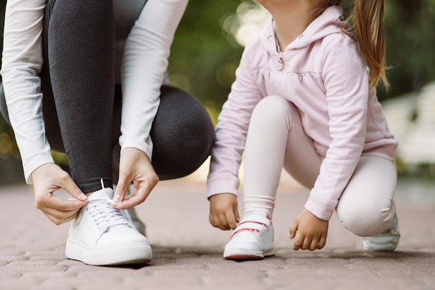 Bijgesneden opname van moeder en dochter die sneakers aanpassen terwijl ze op de joggingbaan in het park zitten