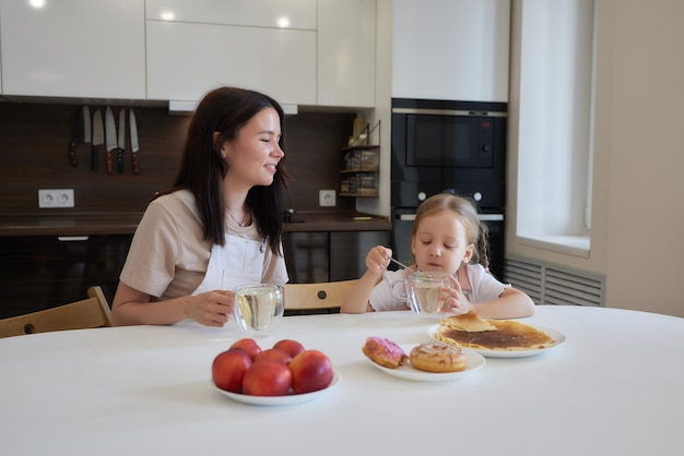 Bijgesneden opname van moeder in het rood en haar dochter met kleurrijke donuts in de keuken Dieetconcept en junkfood