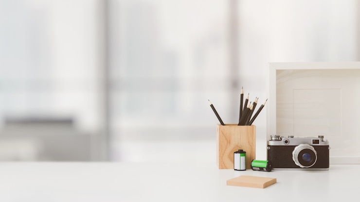 Foto bijgesneden opname van werkruimte met kopie ruimte, camera, briefpapier, frame en boom pot op witte tafel met wazig
