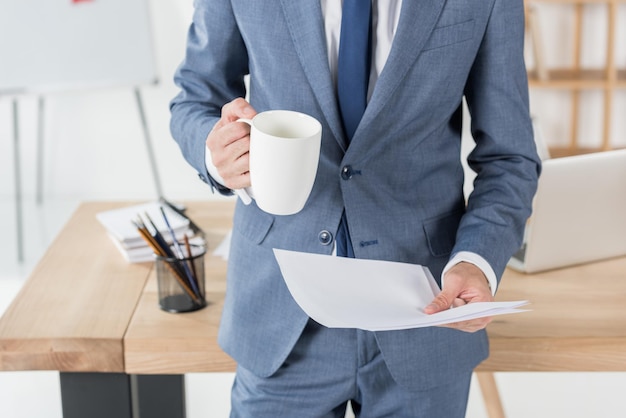 Bijgesneden opname van zakenman met koffiekopje en papieren die op de werkplek staan