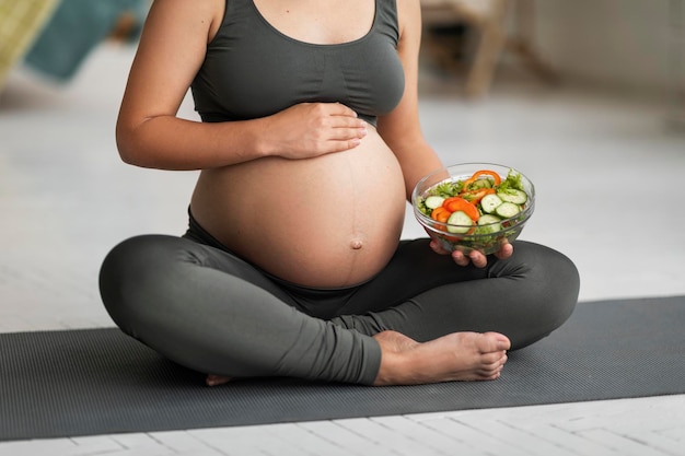 Bijgesneden opname van zwangere vrouw die kom met salade vasthoudt en buik aanraakt