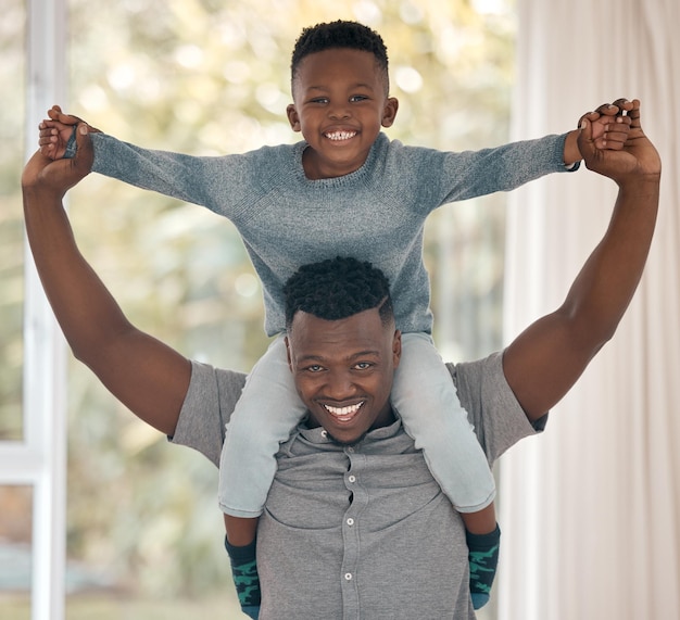 Bijgesneden portret van een knappe jonge man die thuis in de slaapkamer staat met zijn zoon op zijn schouders