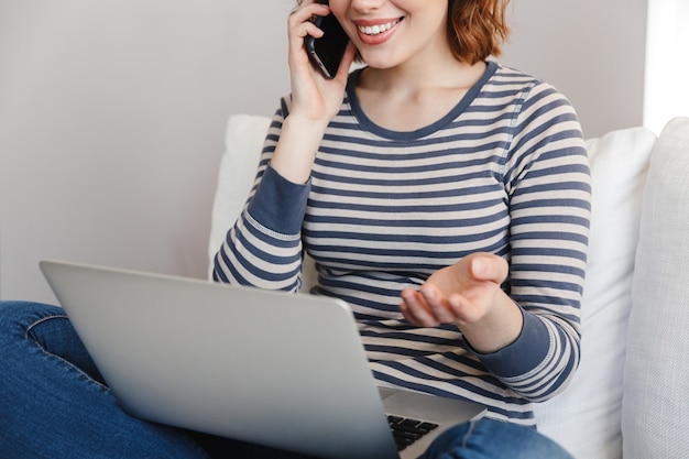 Foto bijgesneden portret van een mooie lachende jonge vrouw ontspannen op een bank thuis, praten op mobiele telefoon