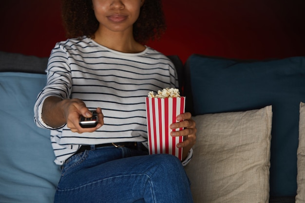 Bijgesneden portret van jonge African American vrouw thuis Tv kijken en popcorn houden zittend op de Bank in een donkere kamer