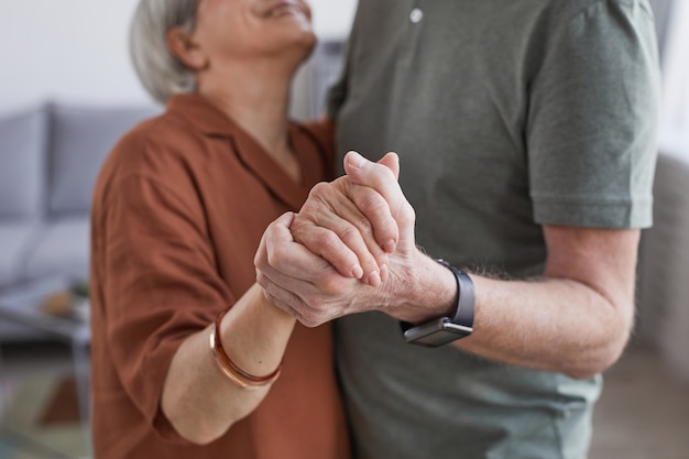 Bijgesneden portret van liefdevol senior koppel dat samen thuis danst en handen vasthoudt