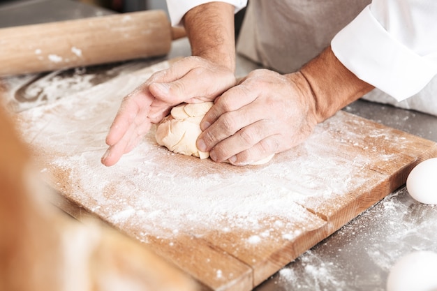 Bijgesneden portret van mannelijke handen die deeg mengen voor gebak, op tafel bij bakkerij of keuken