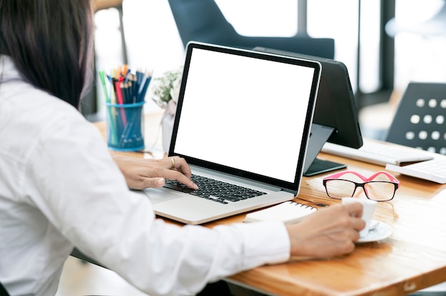 Bijgesneden schot van de hand van de vrouw die op een laptop met een leeg scherm werkt terwijl ze aan haar bureau zit.