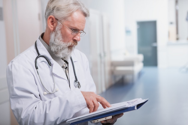 Bijgesneden schot van een senior mannelijke arts te concentreren, het lezen van medische documenten op zijn klembord, kopie ruimte