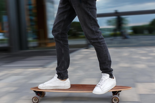 Bijgesneden schot van jonge man in zwarte jeans en witte sneakers rijden op longboard