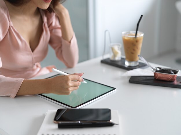 Bijgesneden schot van jonge vrouwelijke schrijven op mock up tablet met lege ruimte in comfortabele kamer