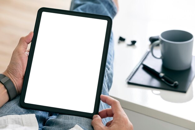 Bijgesneden schot van man handen met behulp van tablet met leeg scherm zittend in de woonkamer thuis.