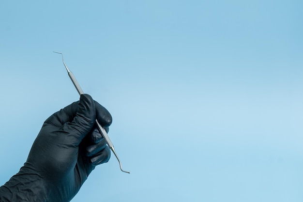 Bijgesneden schot van professionele tandarts in zwarte medische handschoenen met tandheelkundige tool Dental concept geïsoleerd op blauwe achtergrond