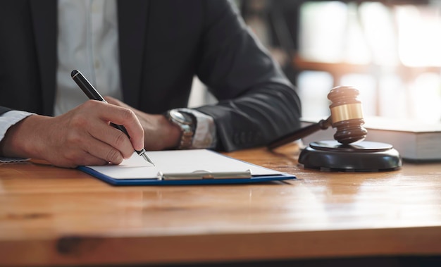 Bijgesneden schot van zakenman hand schrijven notitie zittend aan houten tafel met rechter hamer.