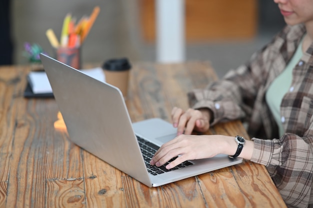 Bijgesneden shot vrouwelijke ontwerper met behulp van laptopcomputer op houten tafel.