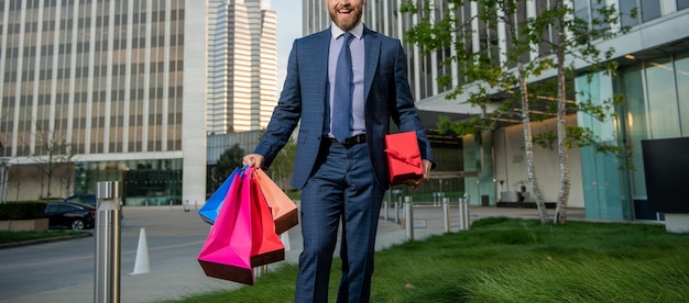 Bijgesneden succesvolle man in formalwear met boodschappentassen en huidige doos buiten de kantoorbonus