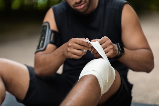 Bijgesneden van atleet zittend op de grond gewonde knie omwikkeld