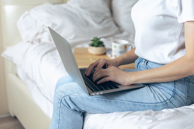 Bijgesneden vrouw typen op laptop zitten op bed thuis kantoor