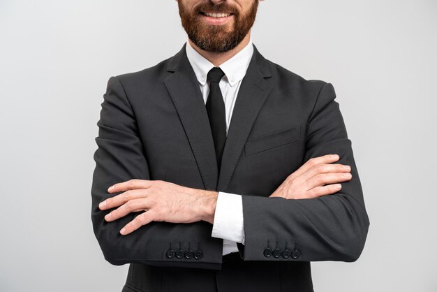 Bijgesneden weergave van de stijlvolle blanke zakenman die naar de camera kijkt met een kalme, zelfverzekerde uitdrukking terwijl hij zijn armen gekruist in de studio poseert