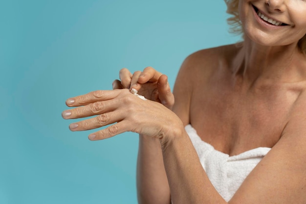 Bijgesneden weergave van een blanke volwassen vrouw die hydraterende crème op haar handen aanbrengt op een blauwe achtergrond