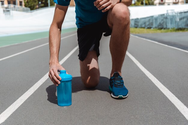 bijgesneden weergave van jonge sportman op atletiekbaan met blauwe bidon