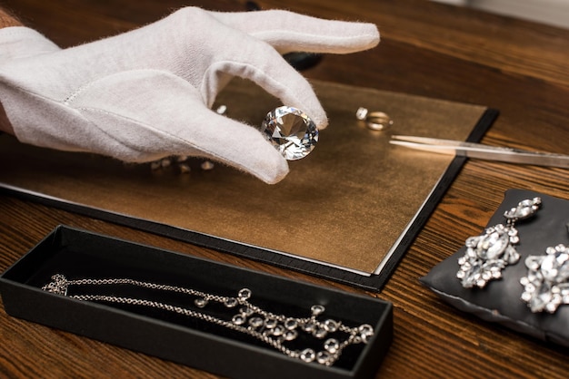 Bijgesneden weergave van sieraden taxateur met edelsteen in de buurt van sieraden aan boord op tafel geïsoleerd op grijs