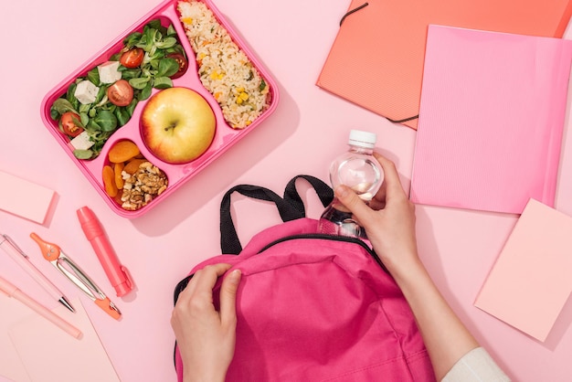 Bijgesneden weergave van vrouw die rugzak inpakt in de buurt van lunchbox en briefpapier