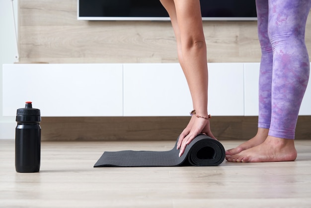 Foto bijgesneden weergave van vrouw die zwarte yoga- of fitnessmat opvouwt na thuis in de woonkamer te hebben gesport