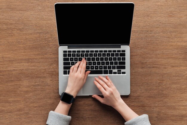 Bijgesneden weergave van vrouw typen op laptop toetsenbord op houten achtergrond