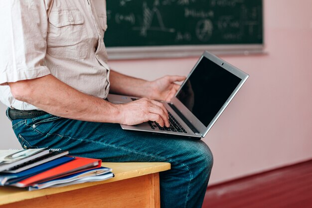 Foto bijsnijdend beeld van leraar die open laptop houdt en op de lijst zit.