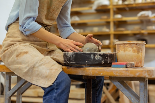 Bijzonder aardewerk wiel. Hardwerkende dame in spijkerbroek zittend op een houten bankje en bezig met aardewerk wiel