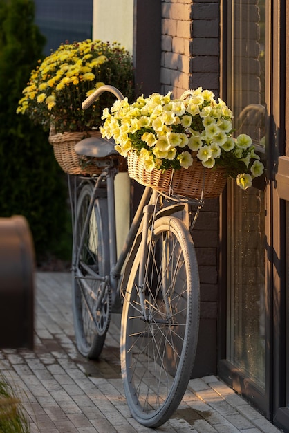 The bike is painted grey It has 2 baskets with yellow flowers House facade decor